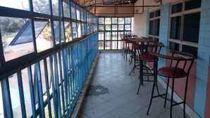 A covered outdoor seating area with tables and chairs, large windows, and a tiled floor. - Eden Garden Hotel (Wote)