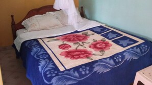 A bed with a floral bedspread, a white mosquito net, and a wooden headboard. - Eden Garden Hotel (Wote)