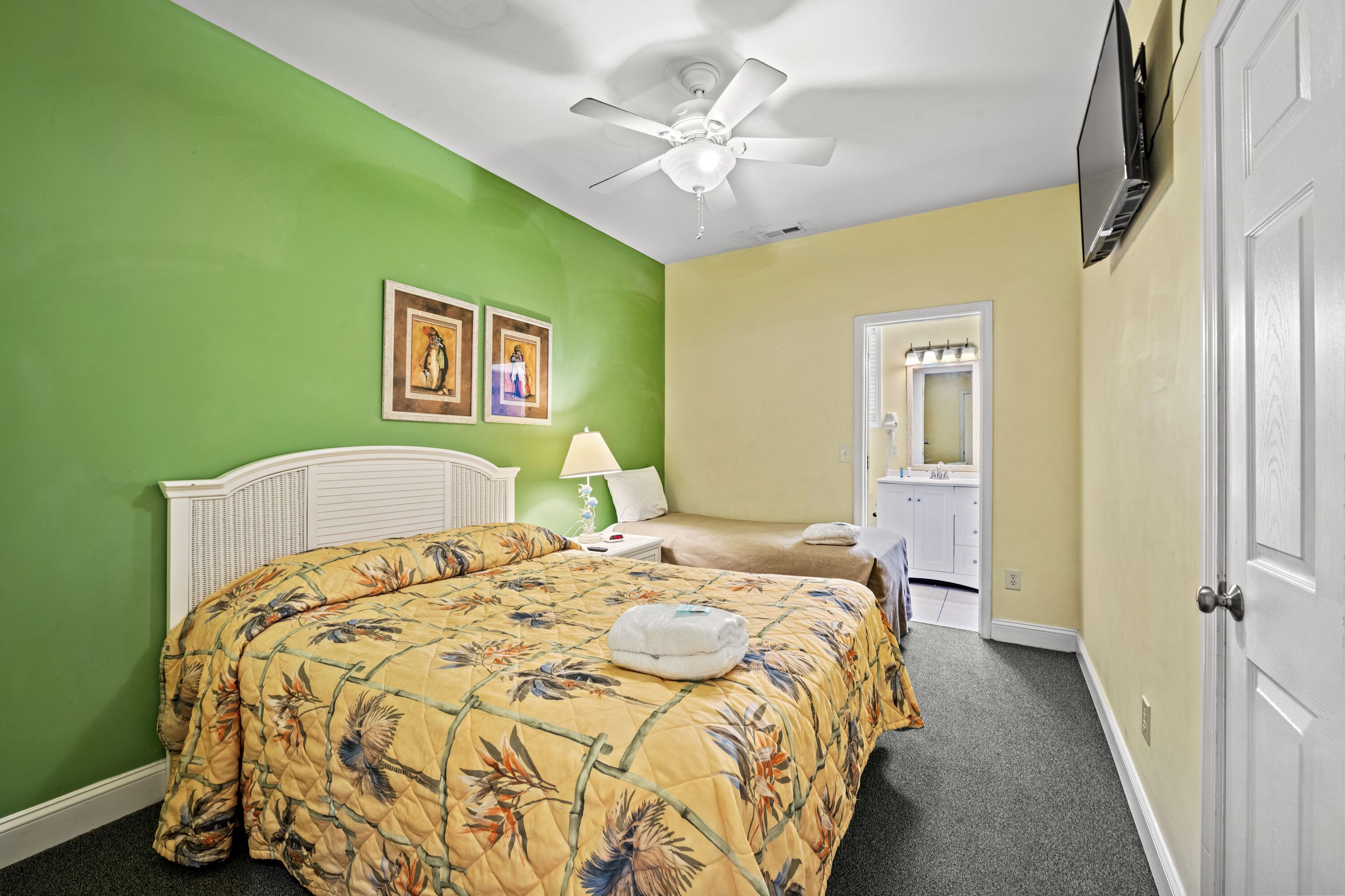 A bedroom with a bed, a ceiling fan, a TV, and a door.