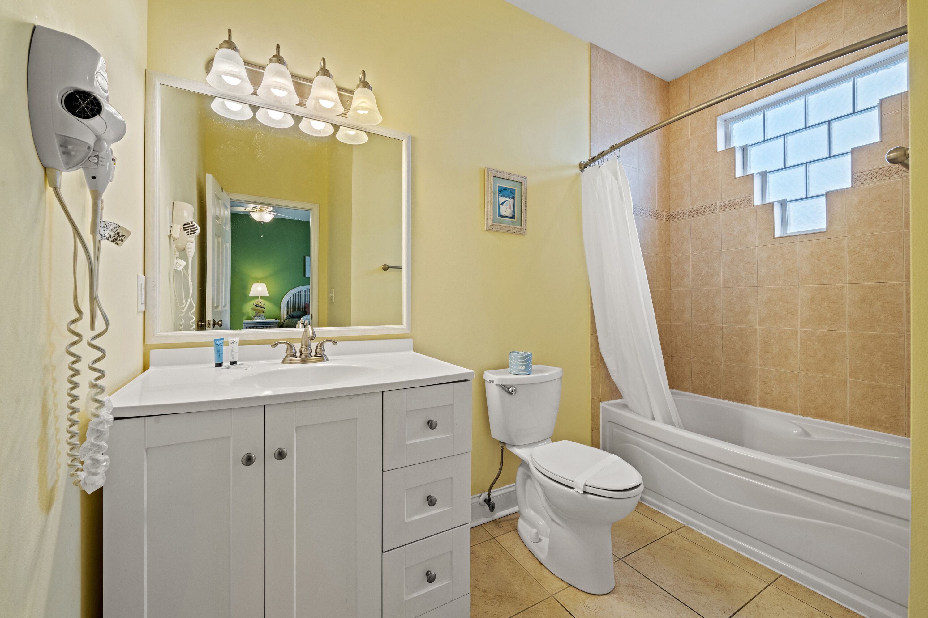 Une salle de bain avec un meuble-lavabo blanc, des toilettes, une baignoire et un sèche-cheveux fixé au mur.