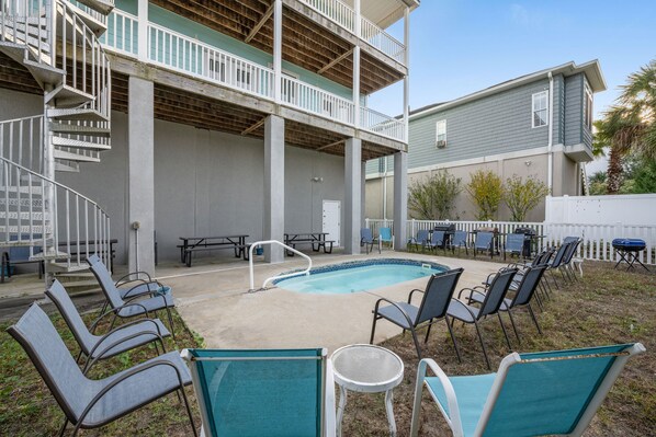 A pool area with lounge chairs, a small table, and a staircase leading to a balcony. - Aqua Paradise: Luxury Beach House with Pool and Game Room (North Myrtle Beach)