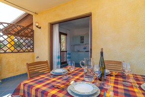 A dining table set with plates, glasses, and a wine bottle, with a view of a kitchen and a wooden lattice structure.
