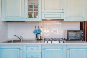 A kitchen with light blue cabinets, a gas stove, a toaster, and a sink.
