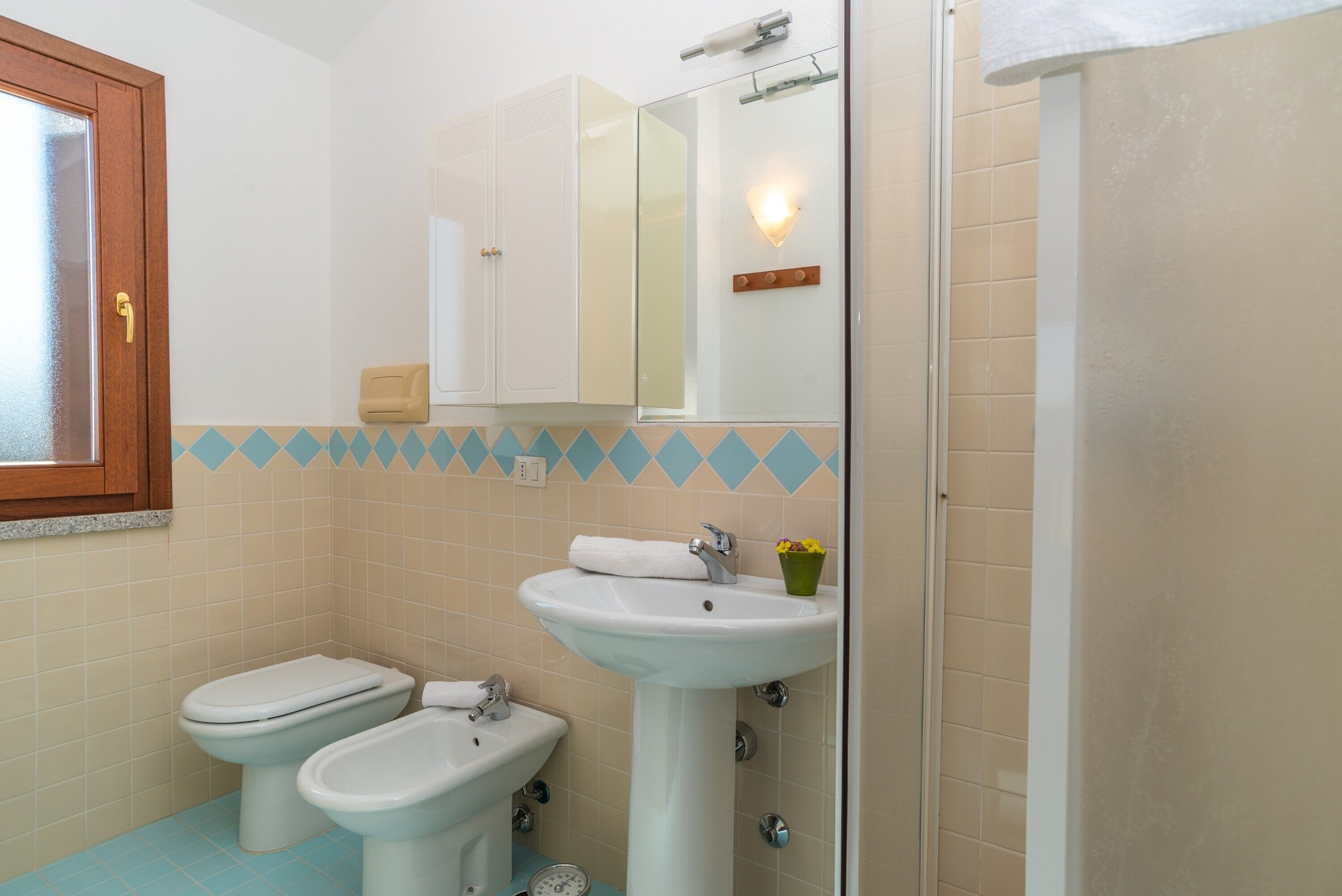 Casa de banho com sanita, bidé, lavatório, espelho e porta-toalhas.