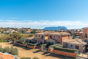 A residential area with terracotta-roofed houses, a clear sky, and distant mountains.