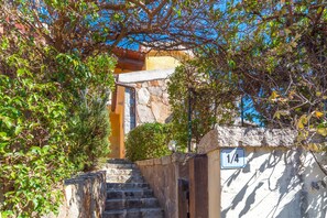 A stone staircase leading to a building entrance, surrounded by greenery and a clear blue sky. - Villa Lucia - Aliterno V6 with Terrace; Parking Available (Olbia)