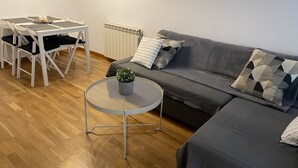 Un soggiorno moderno con un divano grigio, un tavolino rotondo in metallo con una pianta in vaso e un tavolo da pranzo bianco con sedie.