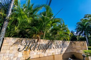A stone wall with the inscription "Hermosa Heights" surrounded by lush green palm trees. - Casa Connie (Sardinal)
