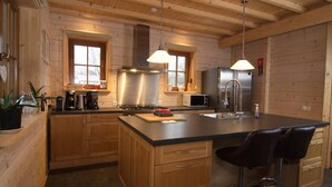 A wooden cabin-style kitchen with a central island, stainless steel appliances, and pendant lighting. - Luxury Wooden Villa Albert in Forested Area with Stunning Countryside Views (Den Ham)