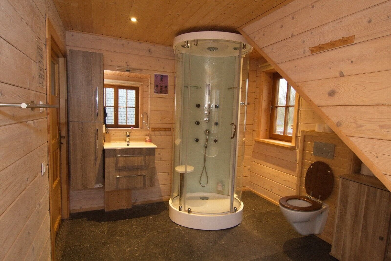 Et badeværelse i en træhytte med et glasafskærmet brusebad, en vask og et toilet.