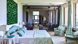 Une chambre moderne avec un grand lit, un coin salon avec des fauteuils, un miroir et une œuvre d’art murale aux tons verts.