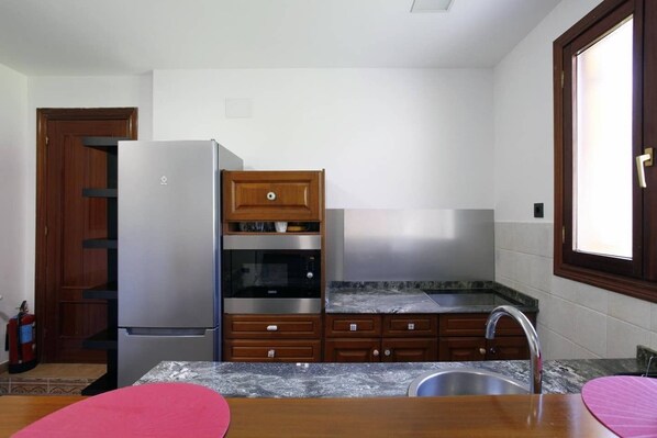 A compact kitchen with a refrigerator, oven, microwave, and wooden cabinets.