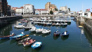 Una marina con numerosas embarcaciones amarradas, rodeada de edificios históricos y una imponente estructura de piedra al fondo.