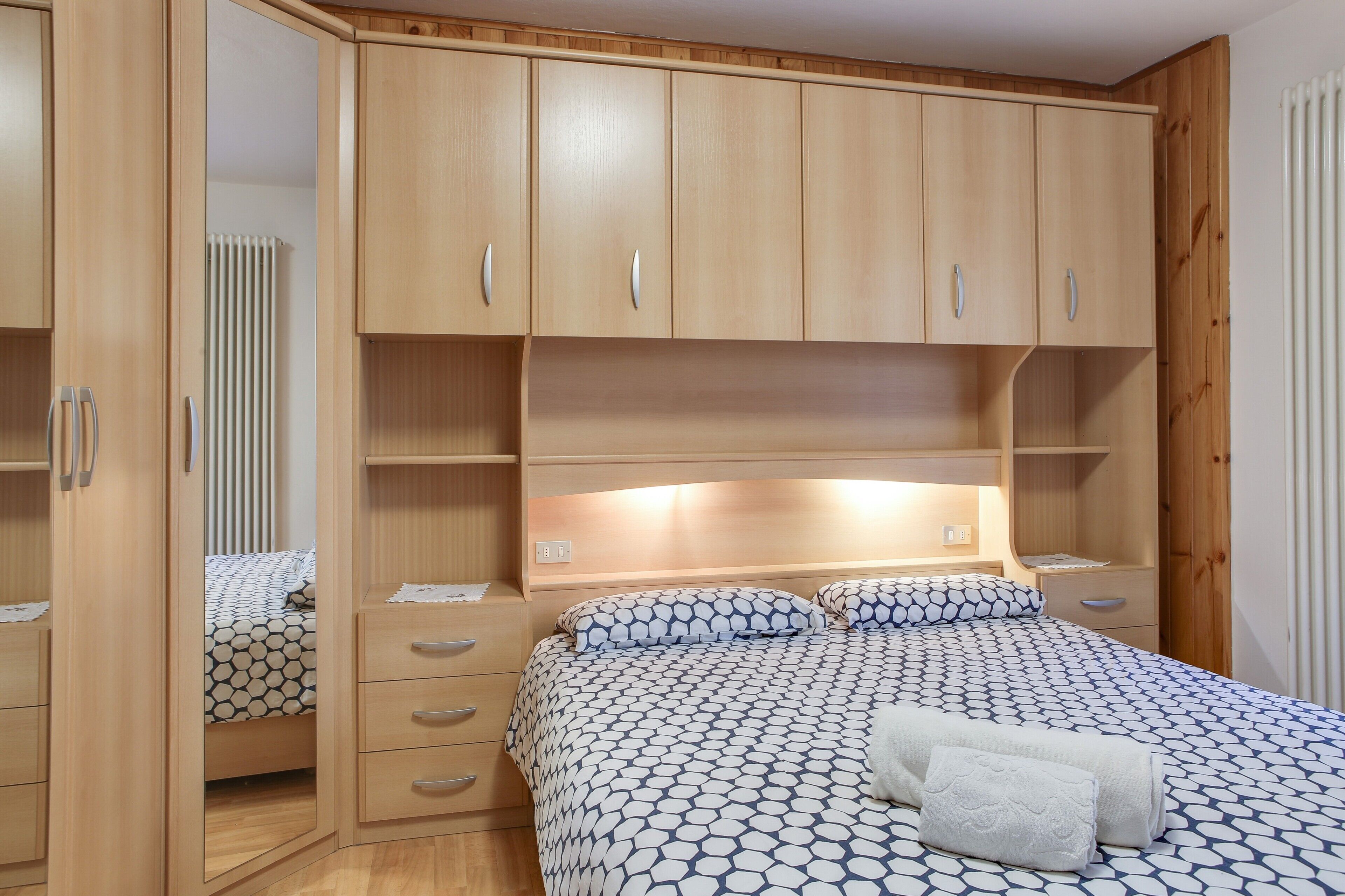Een slaapkamer met een bed, een houten kledingkast en een spiegel.