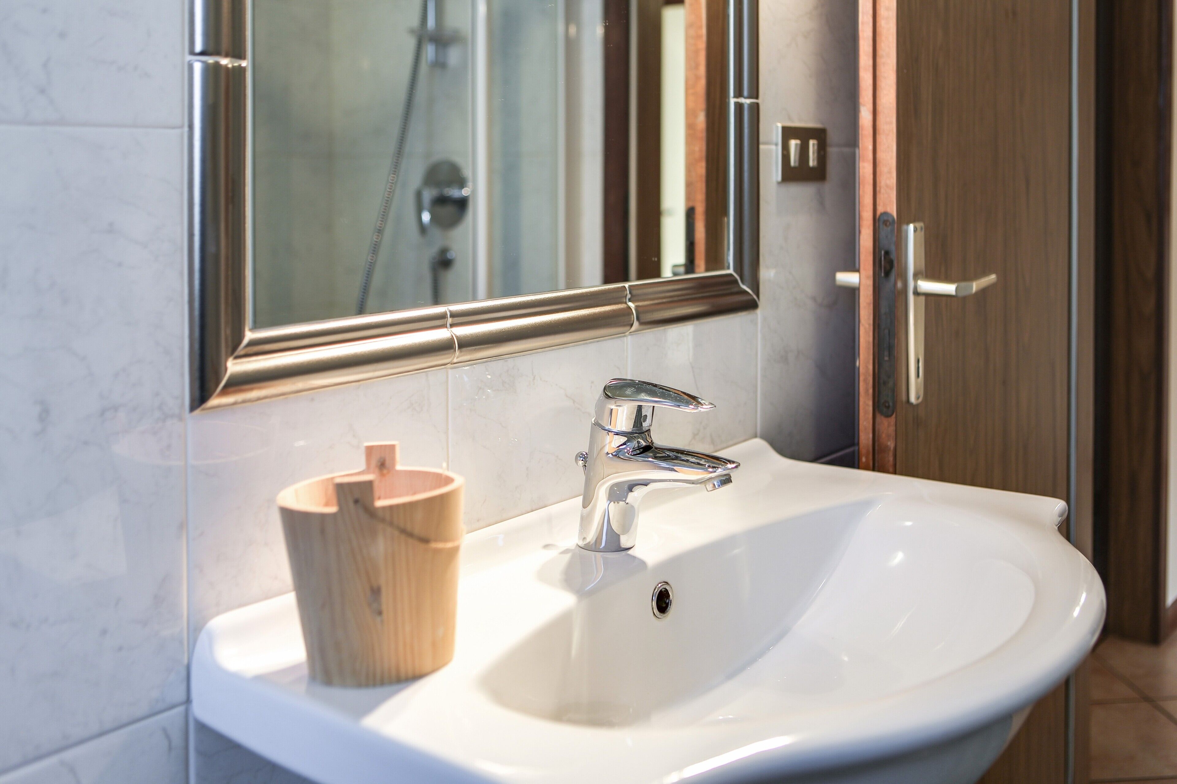 Un baño con un lavabo blanco, un portavasos de madera, un espejo y una ducha a la vista.