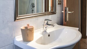 A bathroom with a white sink, a wooden cup holder, a mirror, and a shower visible in the background.