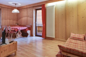 Un interior de madera con una mesa de comedor, sillas, un sofá y un televisor sobre un mueble de madera.