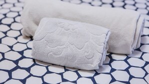 A rolled white towel and a smaller towel on a patterned floor.