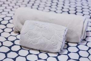 Uma toalha branca enrolada e uma toalha menor sobre um piso estampado.