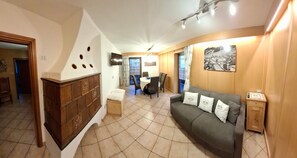 A living room with a sofa, a dining table, and a TV mounted on the wall. - Rustic Apartment Casa March 1 with Wi-Fi, Balcony, Garden & Mountain View (Moena)