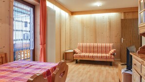 Une pièce au plancher de bois, avec un lit, un canapé, une télévision et une fenêtre avec des rideaux.