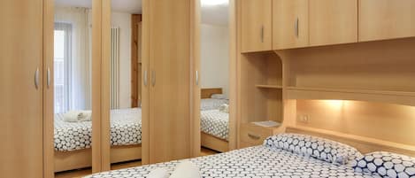 A bedroom with a large bed, a wardrobe with mirrored doors, and a bedside table.
