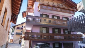 A multi-story building with balconies, a staircase, and a car parked in front.