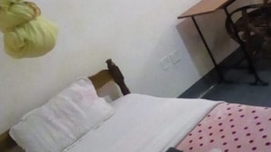 Een enkel bed met een roze stippenbedspreider, een wit kussen en een opgevouwen donkerdeken.
