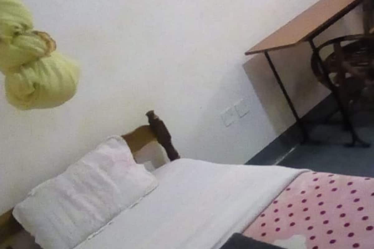 A single bed with a pink polka dot bedspread, a white pillow, and a folded dark-colored blanket.