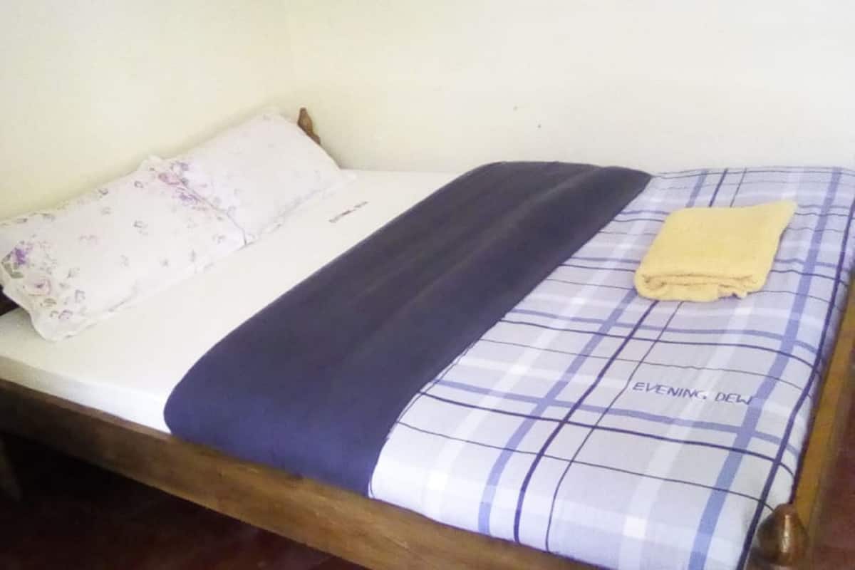 A single bed with a floral pillow, a dark blue blanket, and a yellow towel.