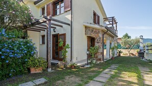 Una casa de dos pisos con fachada de piedra, un balcón de madera y un jardín bien cuidado con plantas en macetas y césped.