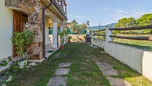 Un edificio de piedra con balcón, plantas en macetas y un jardín cercado.