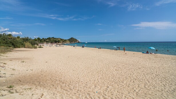 Una amplia playa de arena con cielo azul despejado y mar tranquilo.