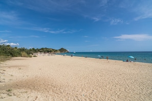 Une vaste plage de sable fin, sous un ciel bleu dégagé et une mer calme.