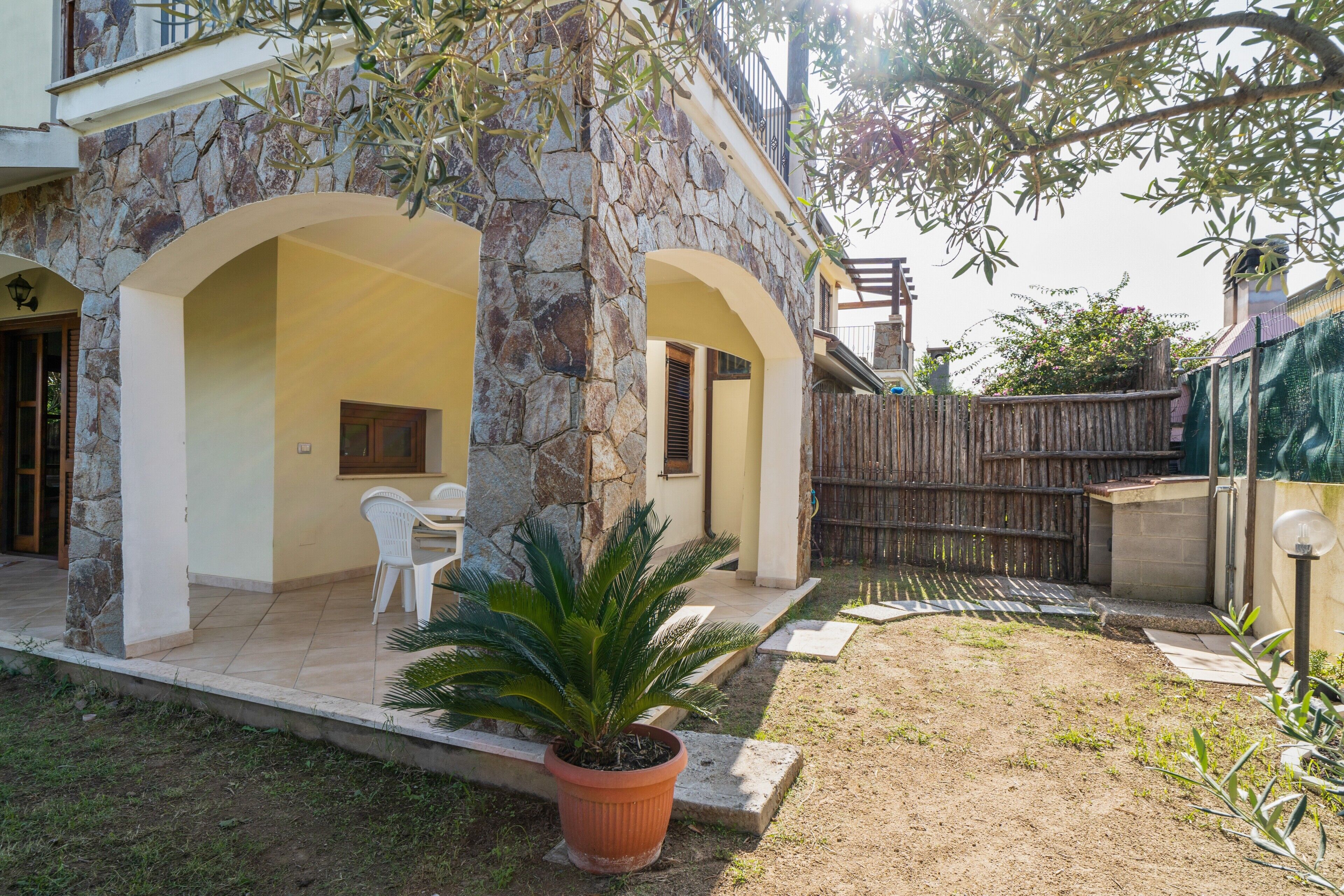 Un edificio de piedra con un patio, sillas blancas y una planta en maceta.
