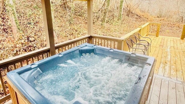 A hot tub on a wooden deck with a wooden railing and chairs.