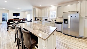 A spacious kitchen with a large island, white cabinetry, stainless steel appliances, and a dining area with chairs and a table.