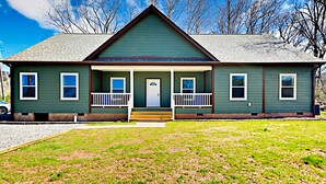 A green house with a front porch, a garage, and a small front yard.