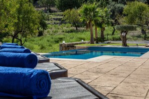 A poolside area with lounge chairs and towels, surrounded by greenery and trees.