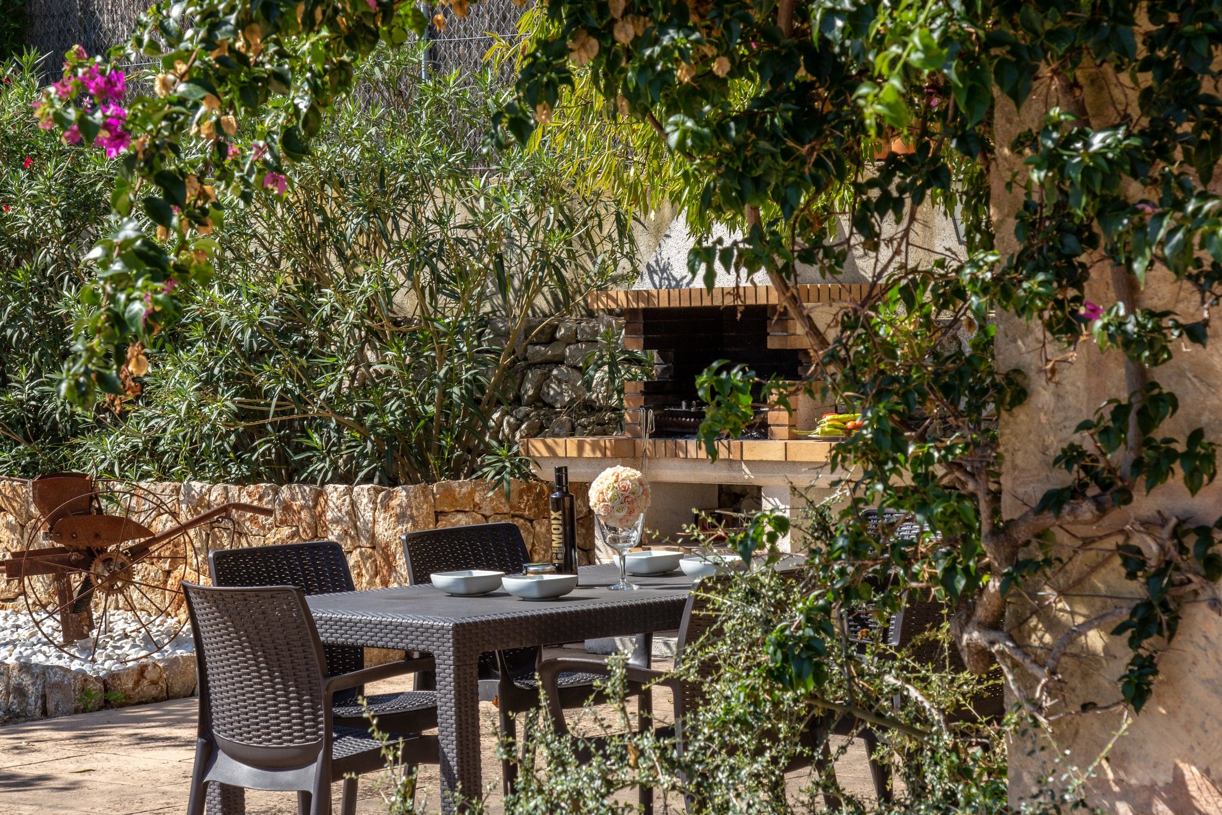 An outdoor dining area with a brick barbecue, wicker chairs, and a stone wall.