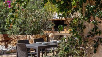 An outdoor dining area with a brick barbecue, wicker chairs, and a stone wall.