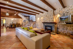 A spacious living area with a stone fireplace, a sofa, and a television mounted on the wall.