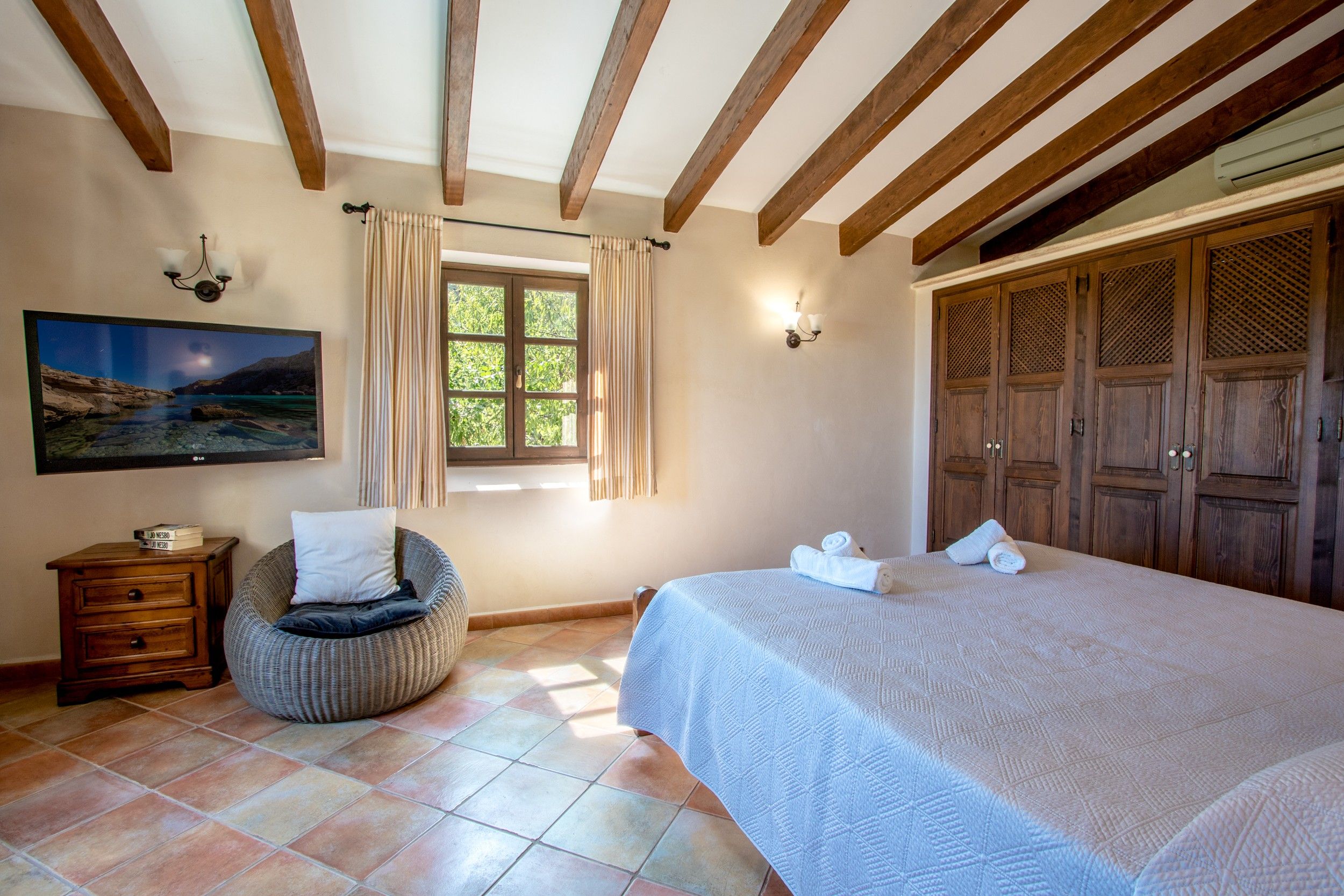 A bedroom with a bed, a chair, a dresser, a painting, and a window with curtains.