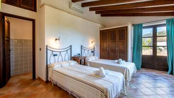 A hotel room with two beds, a wooden ceiling, tiled flooring, a window with curtains, and a door with a wooden panel.