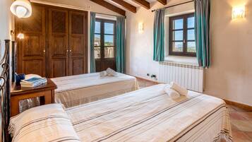 A hotel room with two beds, wooden wardrobe, a bedside table with a lamp, and a window with curtains.
