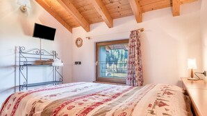A bedroom with a bed, a TV mounted on the wall, a window with curtains, and a wooden ceiling. - Apartment 'Dimora La Quiete' with Mountain View, Private Terrace and Balcony (Bedollo)