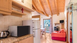 A compact kitchen with a microwave, refrigerator, and kettle, a dining area with a table and chairs, and a red sofa in a living space. - Apartment 'Dimora La Quiete' with Mountain View, Private Terrace and Balcony (Bedollo)