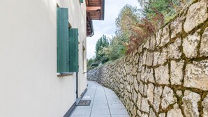 A narrow stone-walled pathway leading to a building with green shutters. - Apartment 'Dimora La Quiete' with Mountain View, Private Terrace and Balcony (Bedollo)