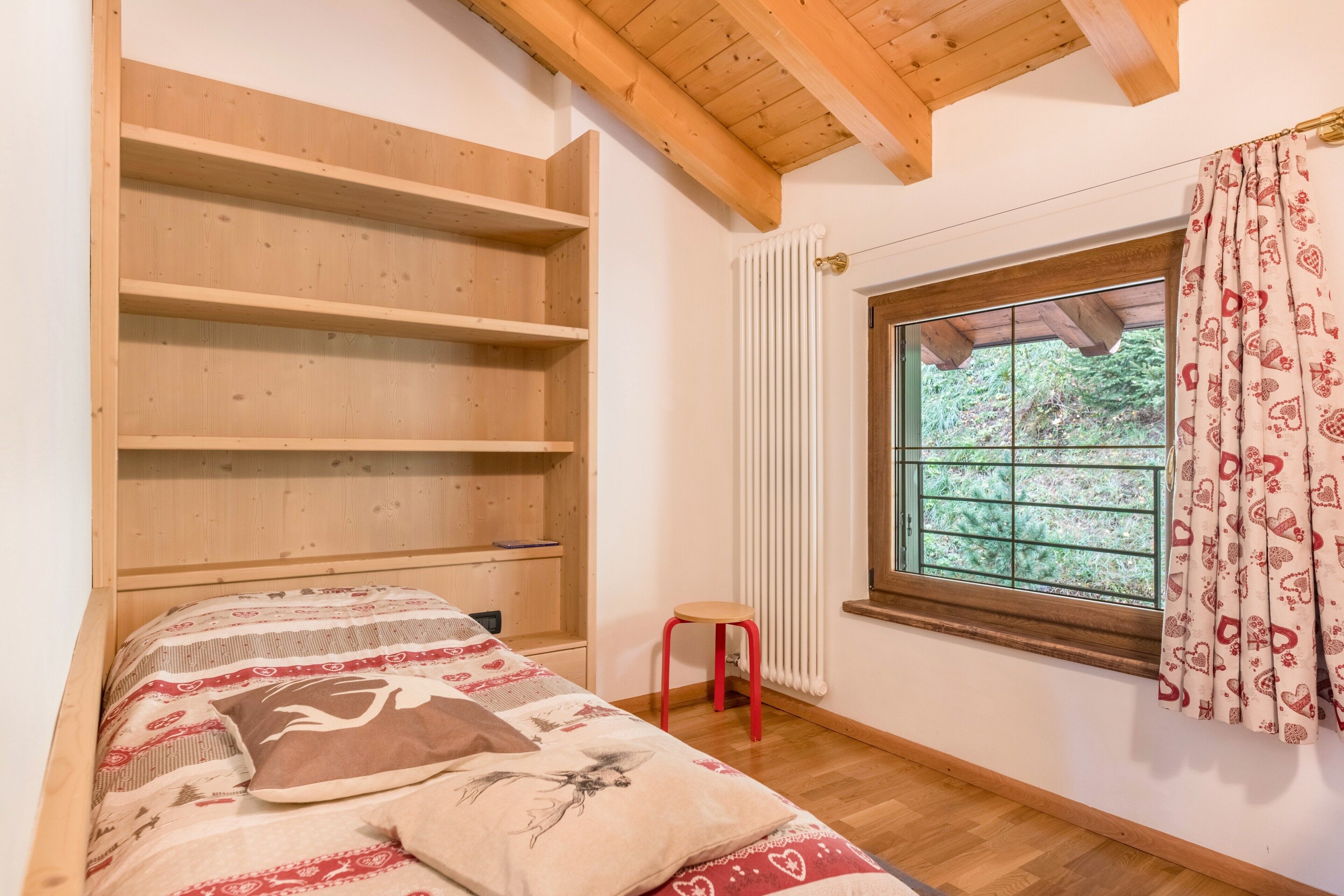 Ein Schlafzimmer mit Bett, Holzregalen, einem Fenster mit Vorhängen und einer Heizung.