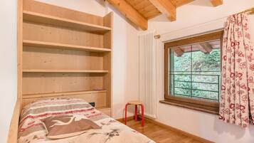 Ein Schlafzimmer mit Bett, Holzregalen, einem Fenster mit Vorhängen und einer Heizung.